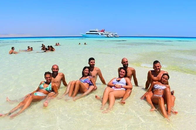 Two couples relaxing together in shallow turquoise water with a white cruise boat anchored in the background