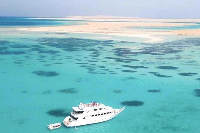 Aerial view of a white yacht anchored near dark coral patches close to a bright white sandbar island